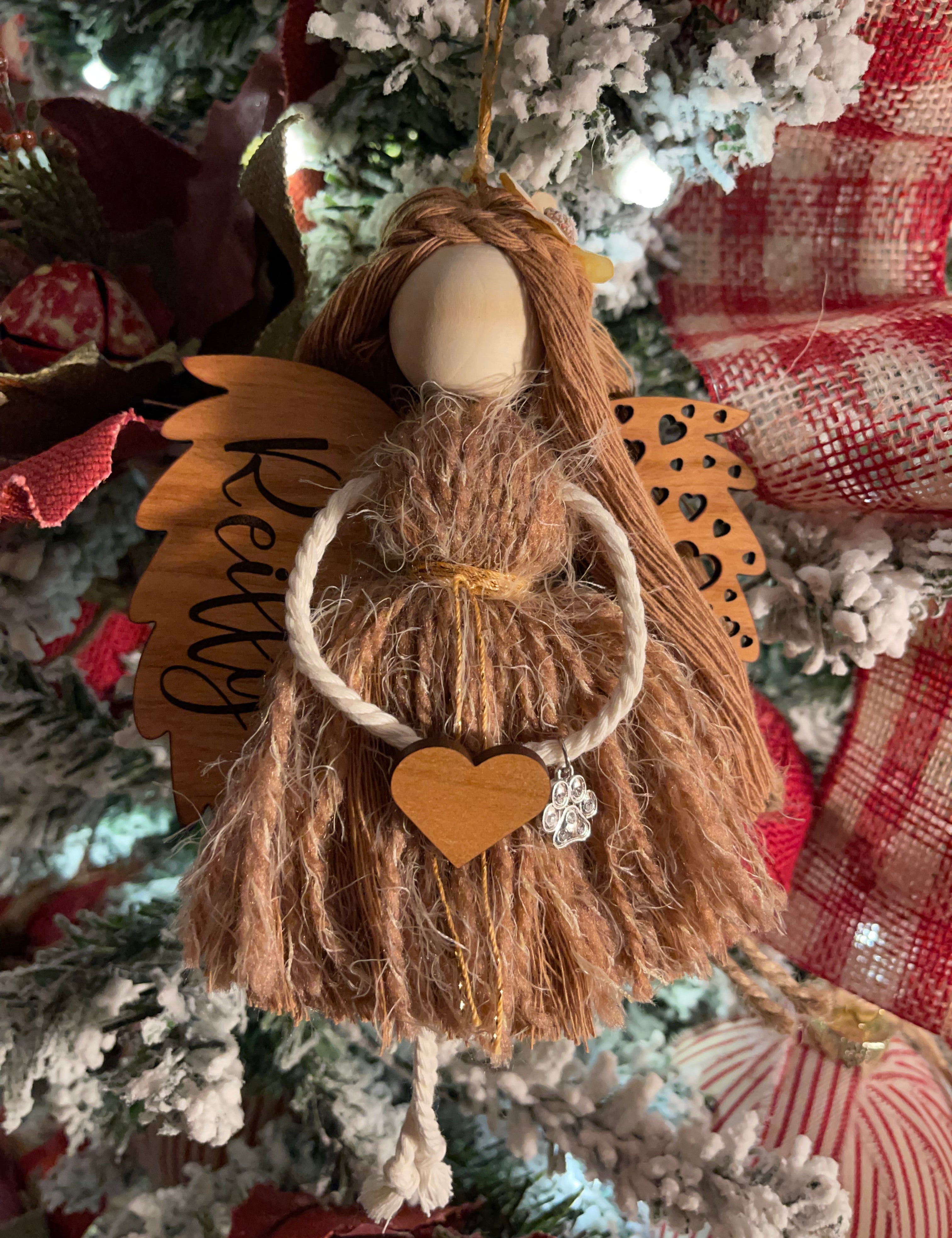 This image shows the angel hanging on a Christmas tree with the engraved name Reilly. The angel is holding a wooden heart and has a paw charm on the arm.