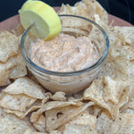 Dip in a glass bowl surrounded by tortilla chips on a wooden board.