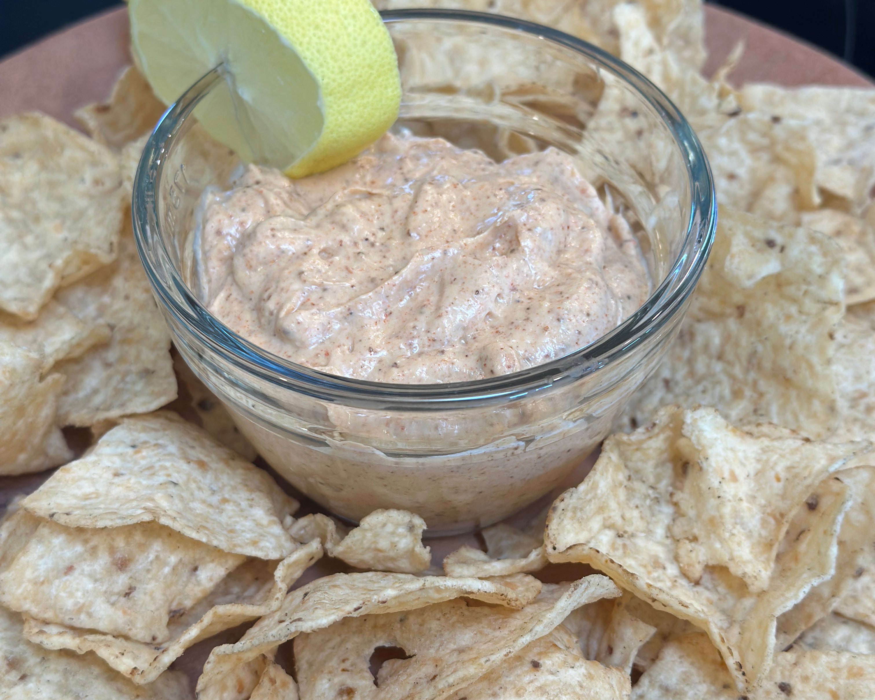 Dip in a glass bowl surrounded by tortilla chips on a wooden board.