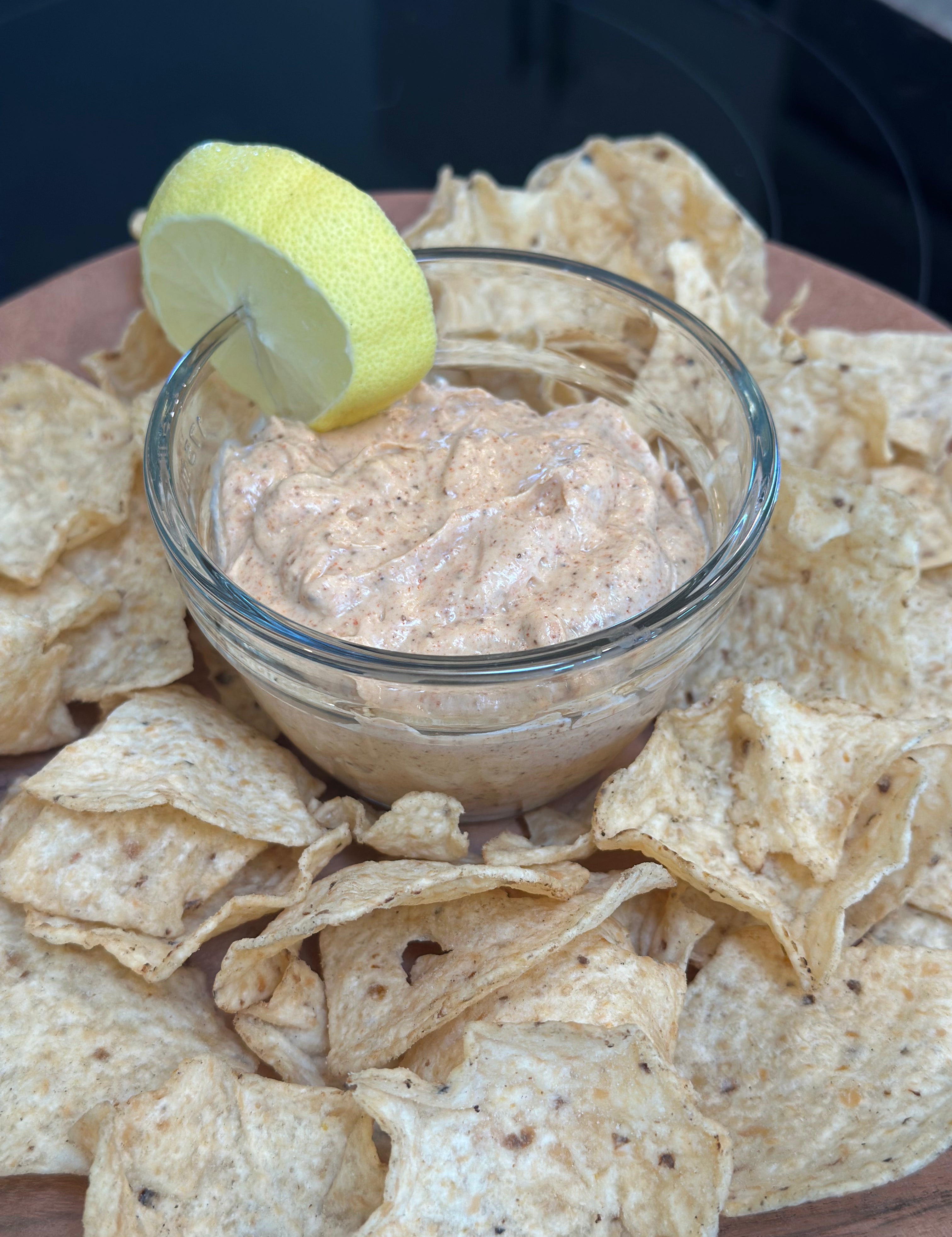 Dip in a glass bowl surrounded by tortilla chips on a wooden board.