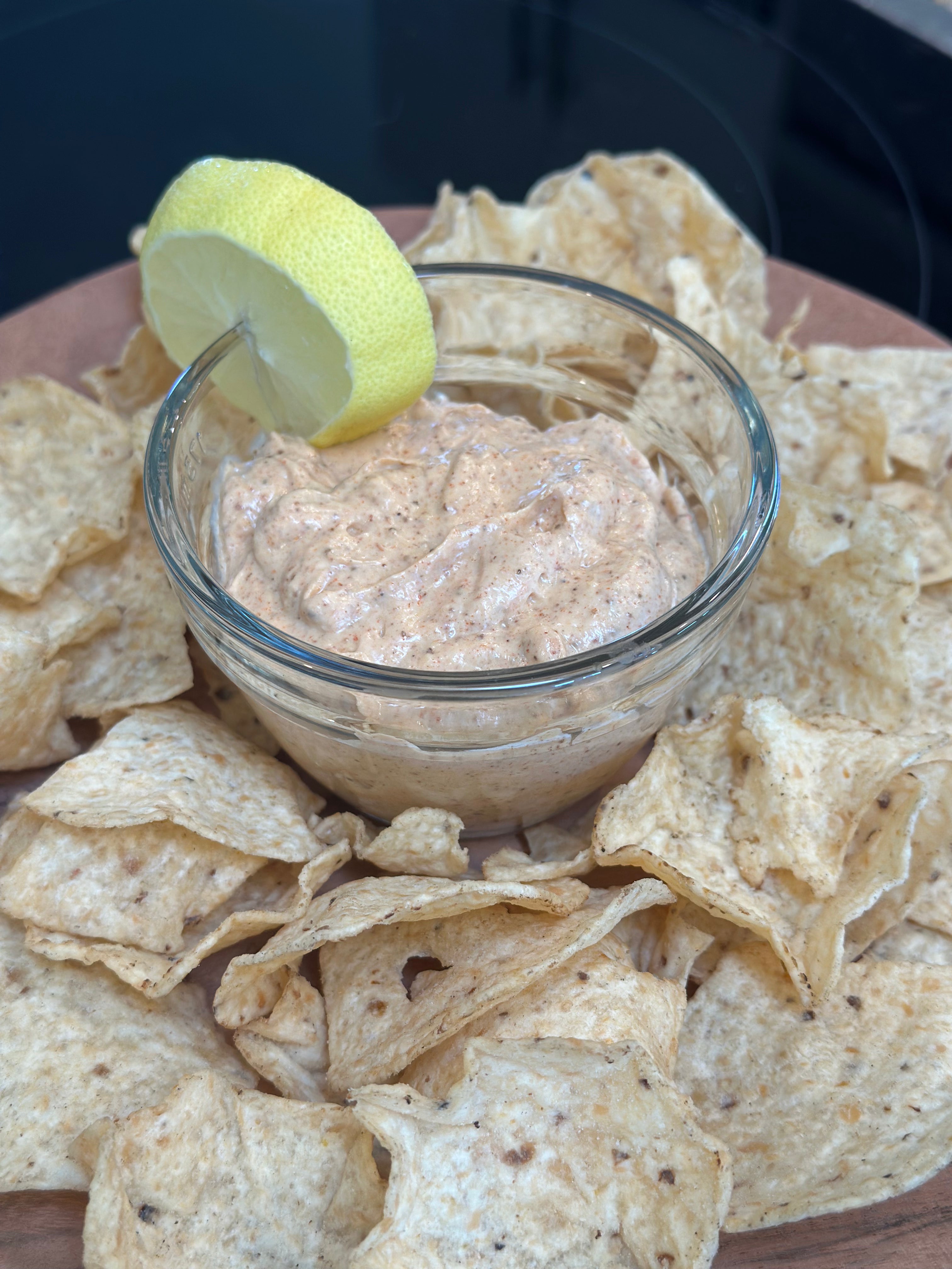 Dip in a glass bowl surrounded by tortilla chips on a wooden board.