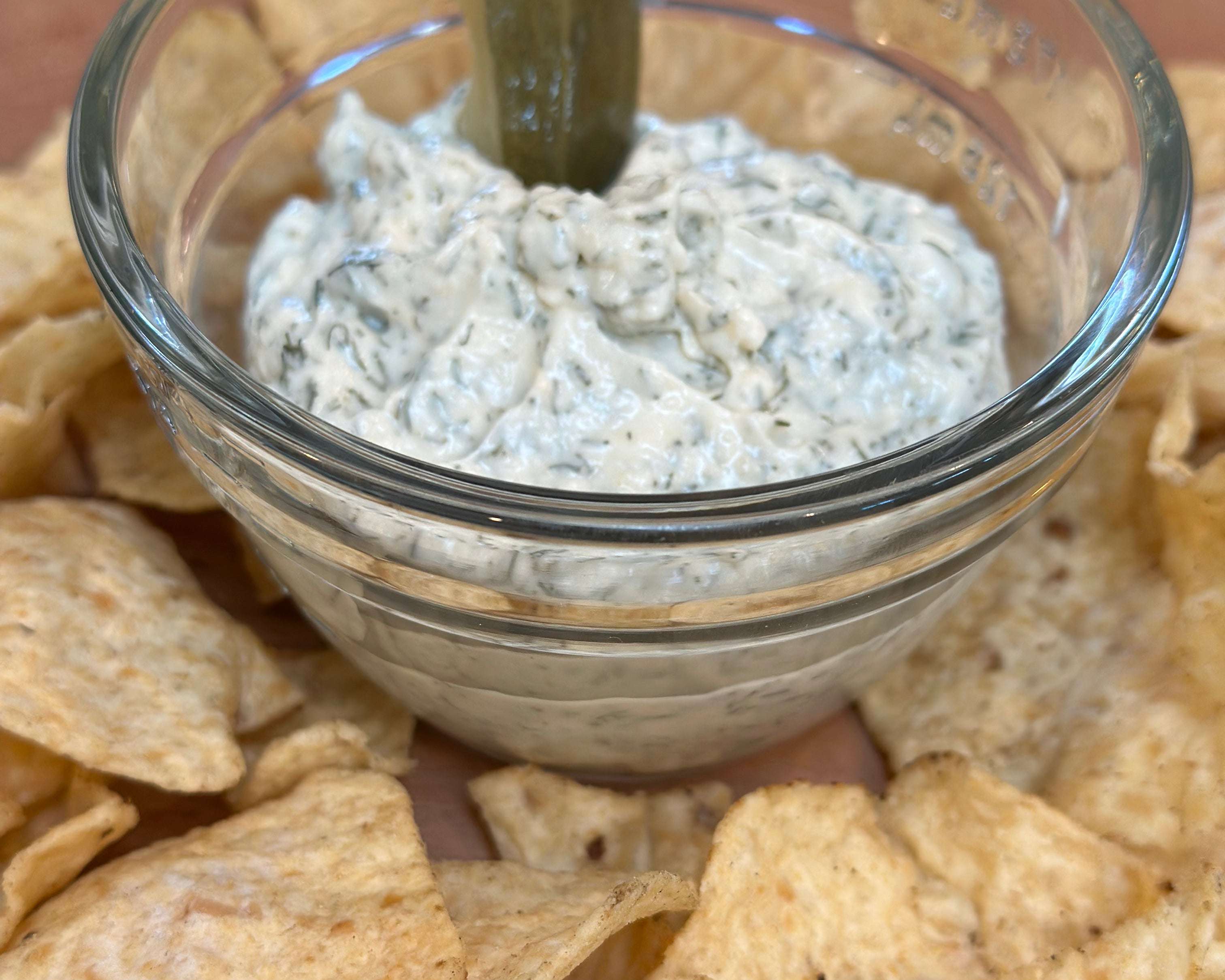 Glass bowl of dip with tortilla chips on a wooden surface