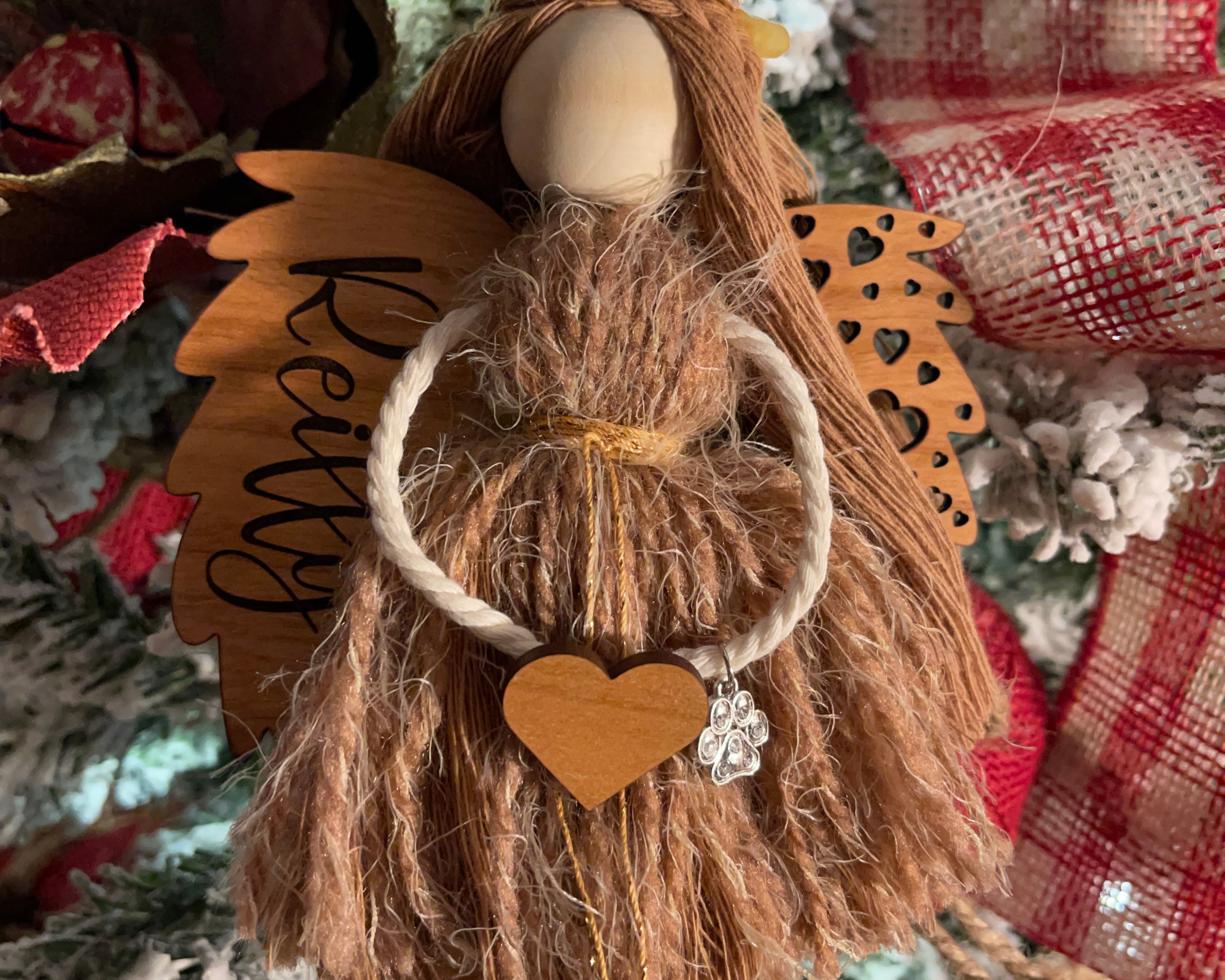 This image shows the angel hanging on a Christmas tree with the engraved name Reilly. The angel is holding a wooden heart and has a paw charm on the arm.