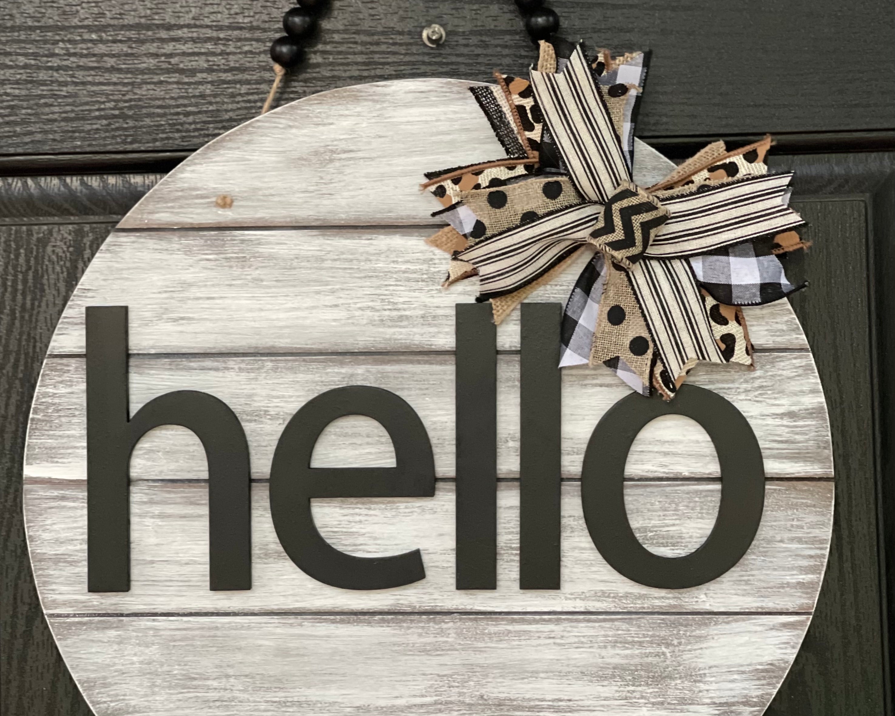 Hello Door Hanger is shown hanging on a front door.  This is the white distressed hanger with black beaded garland.