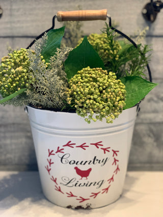 Country Living White Metal Pail is shown with a floral arrangement.  Flowers are not sold with bucket.