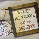 In A World Full of Grinches, Be A Cindy Lou Who 7x7 Sign is shown with the matching ornament.  Each product sold separately.