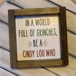 In A World Full of Grinches, Be A Cindy Lou Who 7x7 Sign shows the sign by itself with the word Grinch in green paint and Cindy Lou Who in red paint.