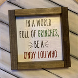 In A World Full of Grinches, Be A Cindy Lou Who 7x7 Sign shows the sign by itself with the word Grinch in green paint and Cindy Lou Who in red paint.