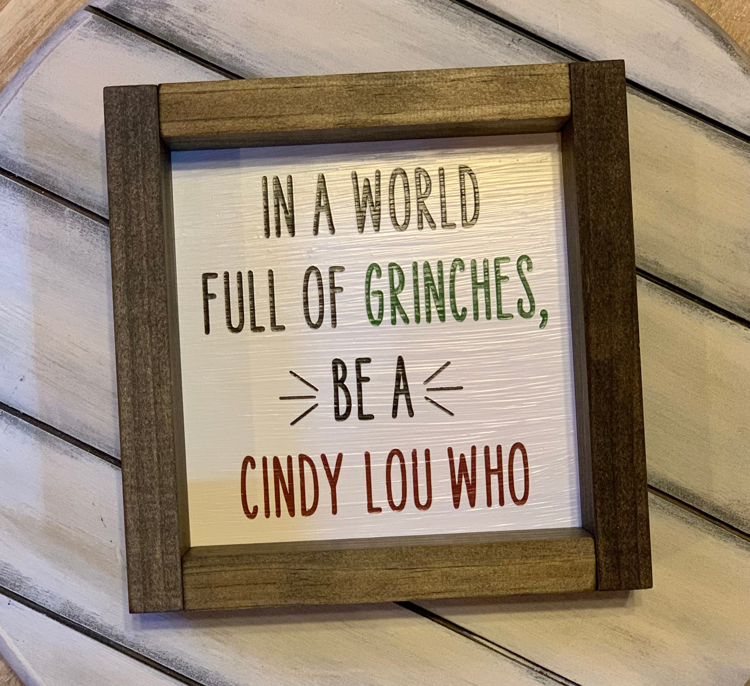 In A World Full of Grinches, Be A Cindy Lou Who 7x7 Sign shows the sign by itself with the word Grinch in green paint and Cindy Lou Who in red paint.