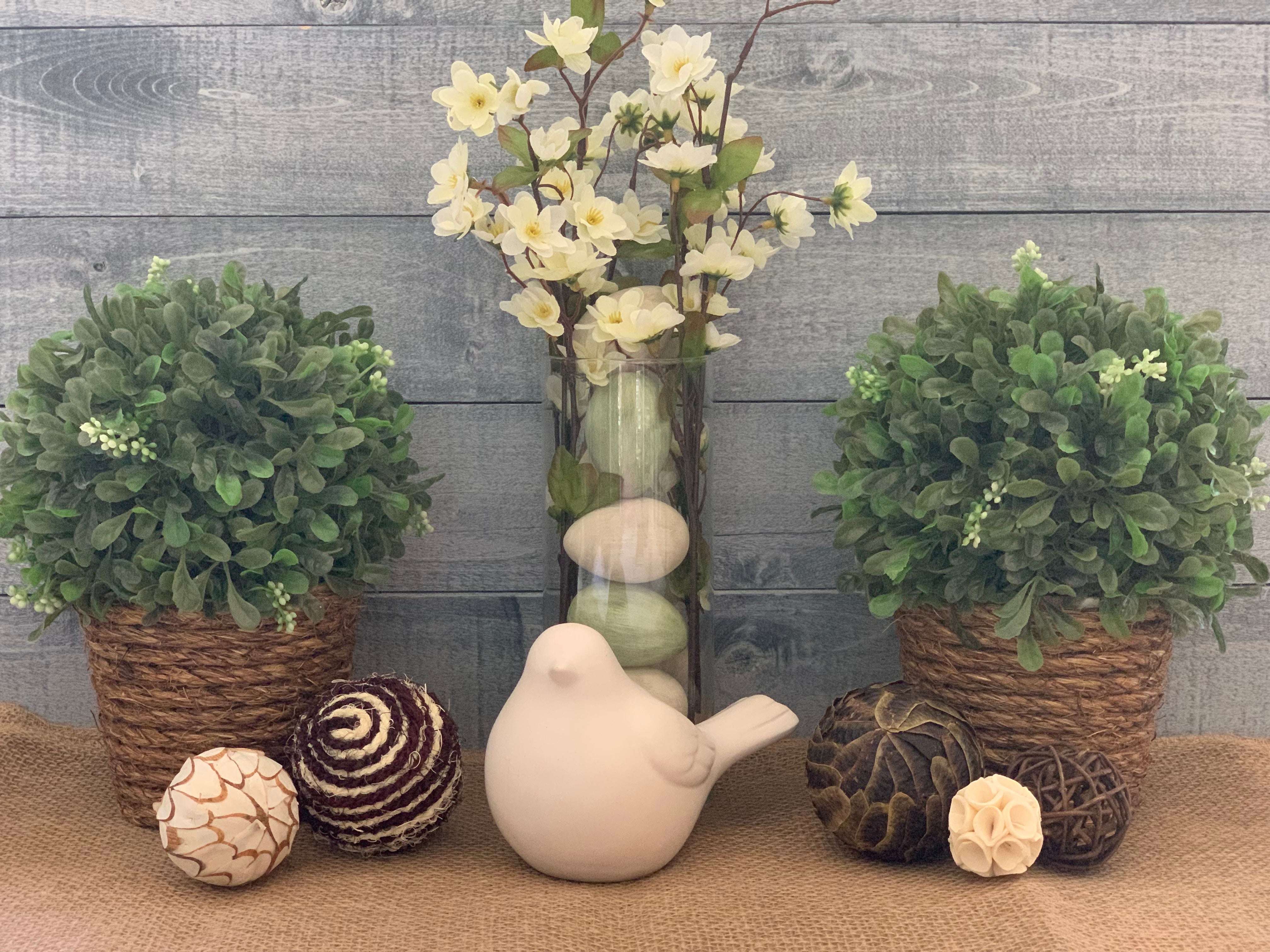 Topiary with Twine Rope shows an image of the topiary sitting on a table as an arrangement with a second topiary, a floral arrangement, a porcelain bird, and decorative balls.