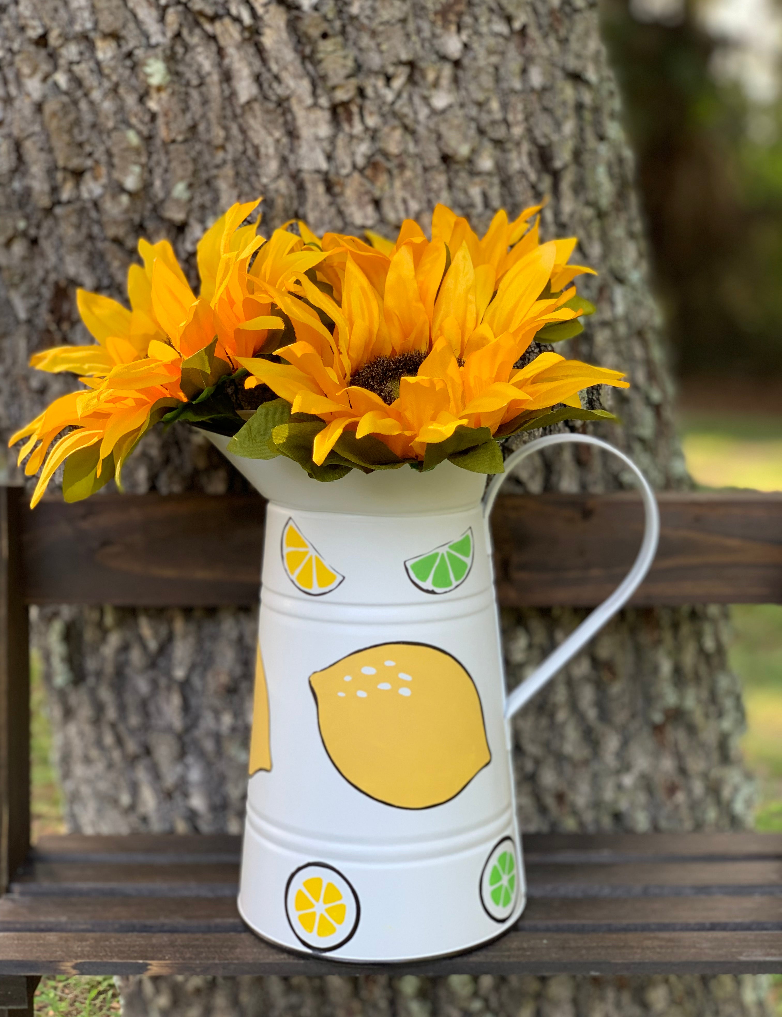White Metal Lemon and Lime Pitcher shows an image of the pitcher with sunflowers sitting on a ladder outside.