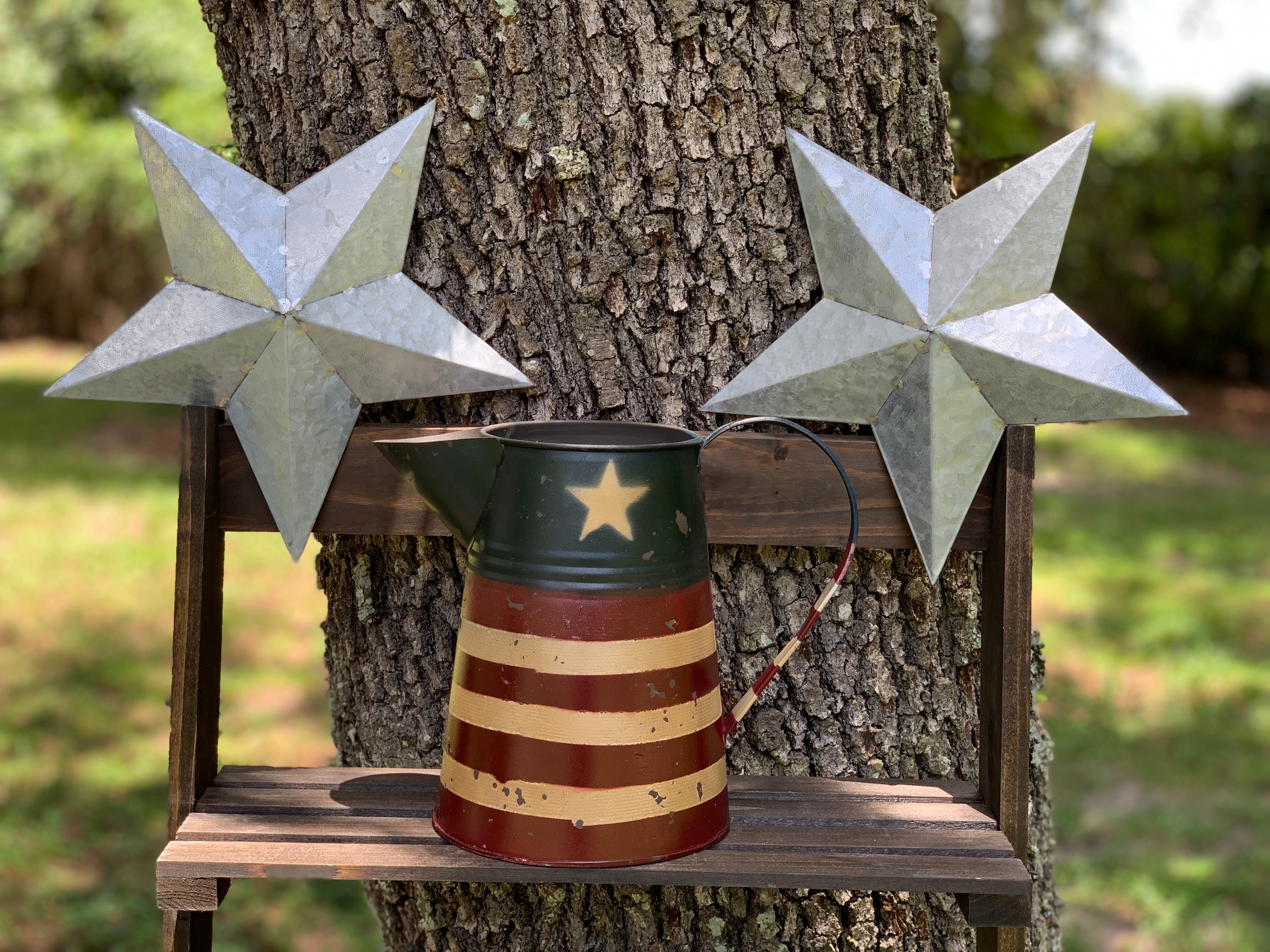 Primitive Red, Tan, and Navy Metal Pitcher is displayed outside sitting on a ladder with metal stars.  Each item sold separately.