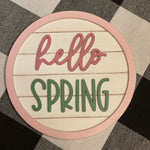 Hello Spring round 5" shiplap sign is shown laying on a table.