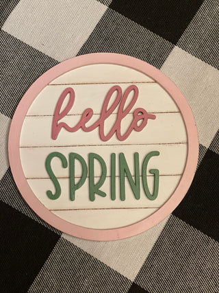 Hello Spring round 5" shiplap sign is shown laying on a table.