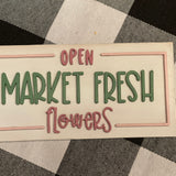 This Market Fresh Flowers Tiered Tray Sign is displayed laying on a table.