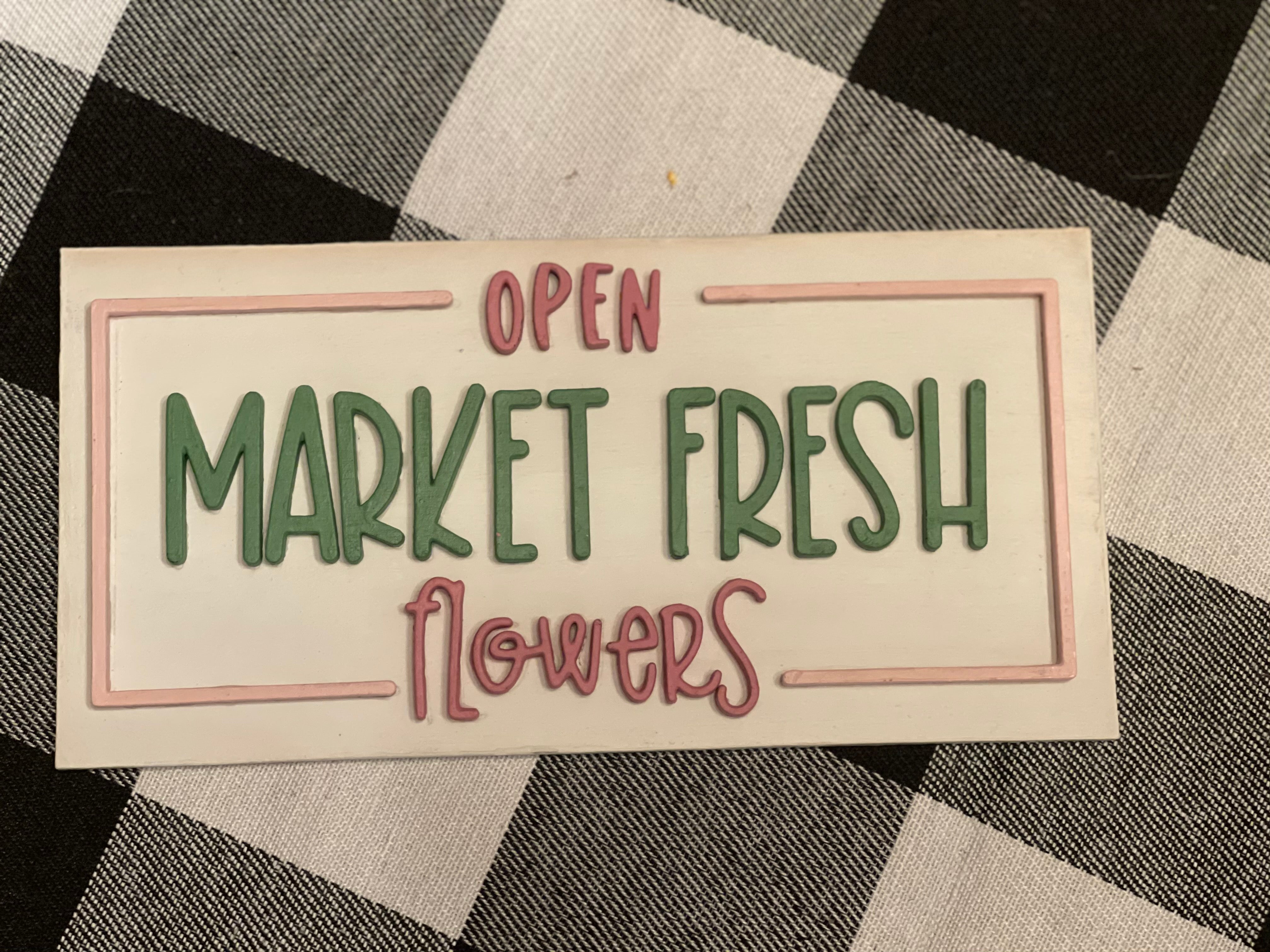 This Market Fresh Flowers Tiered Tray Sign is displayed laying on a table.