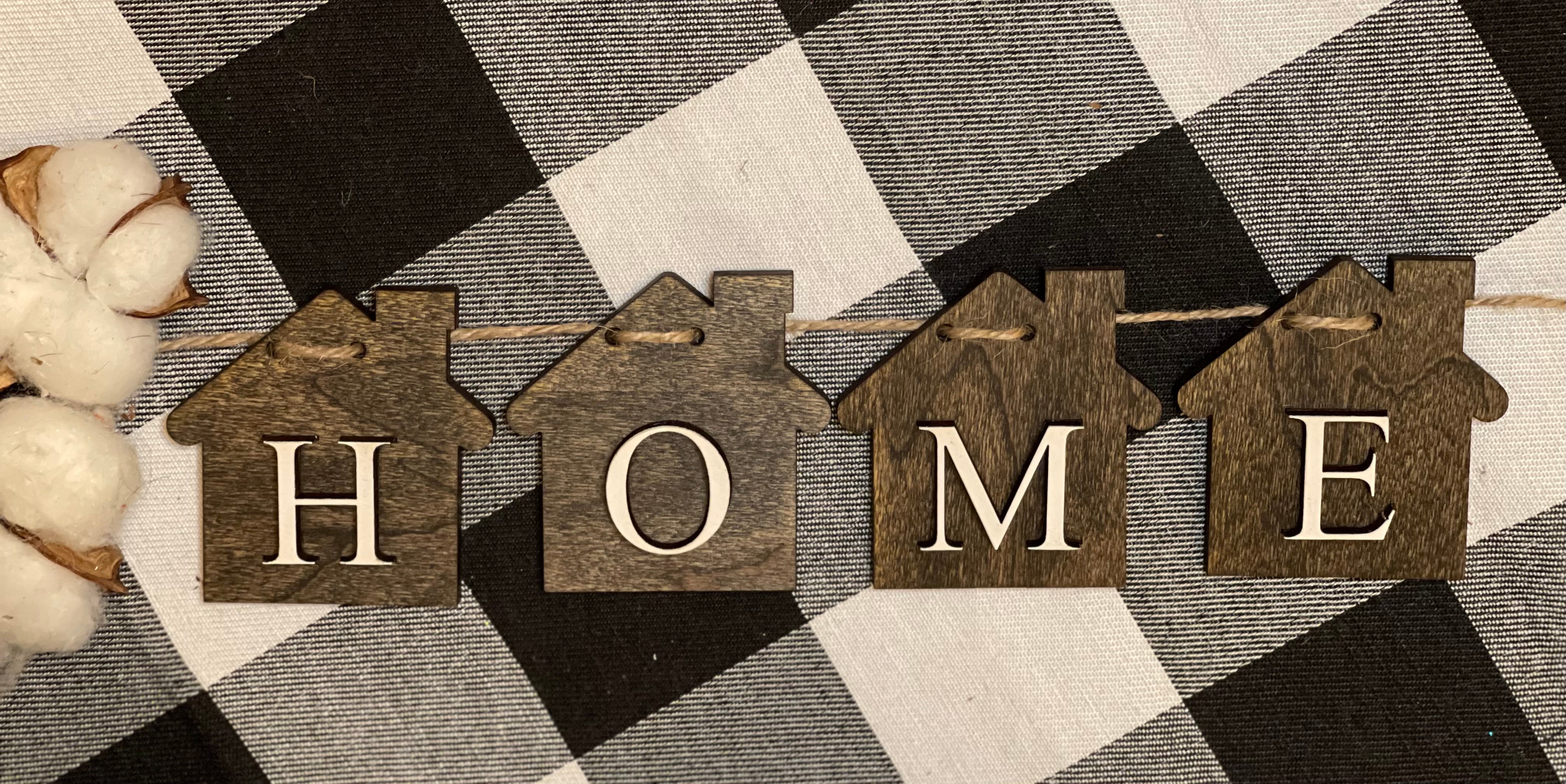 This image show a close up of the home banner.  Jacobean stained wood house cutouts with the letters HOME added to each house.  The banner is 32" from end to end. 