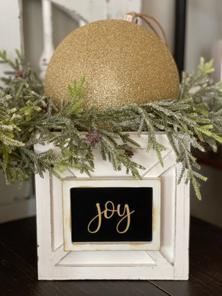 This image shows the Joy gold glitter ornament ball with pine greenery.