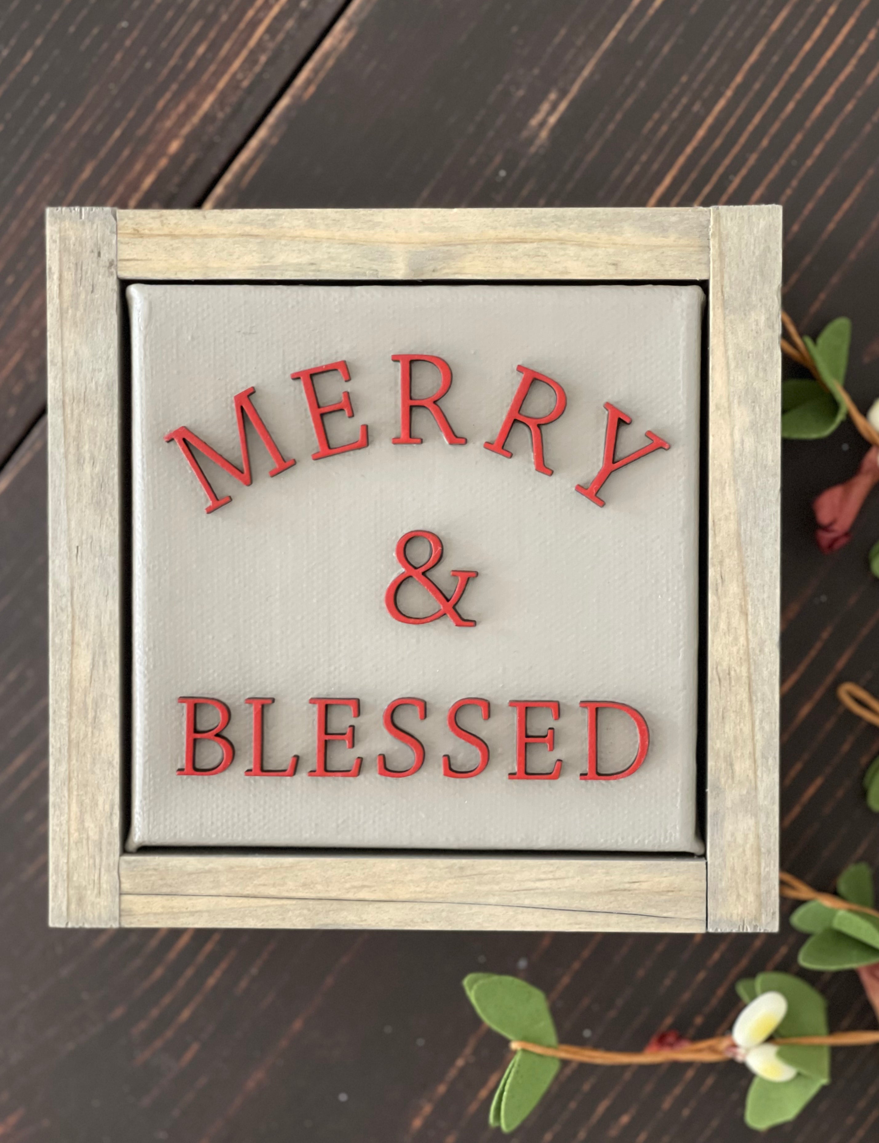 Merry + blessed is displayed on a bench with greenery.