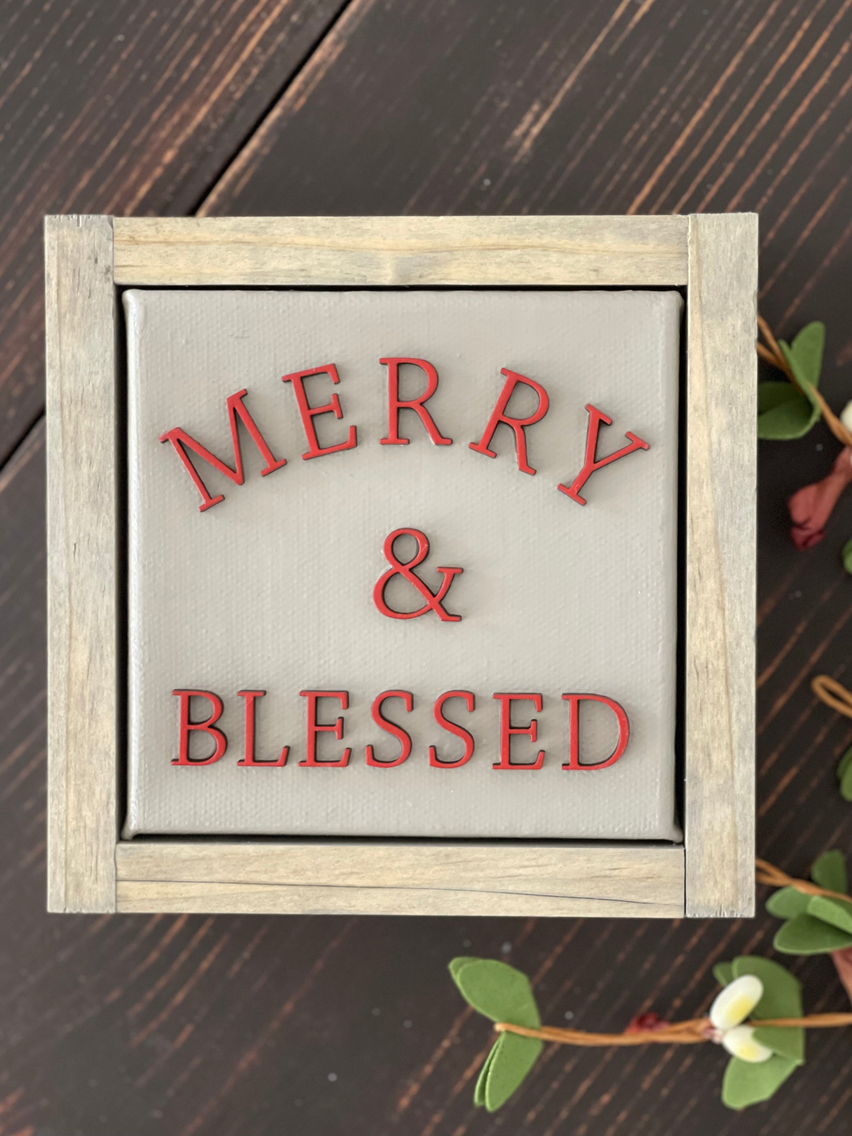 Merry + blessed is displayed on a bench with greenery.