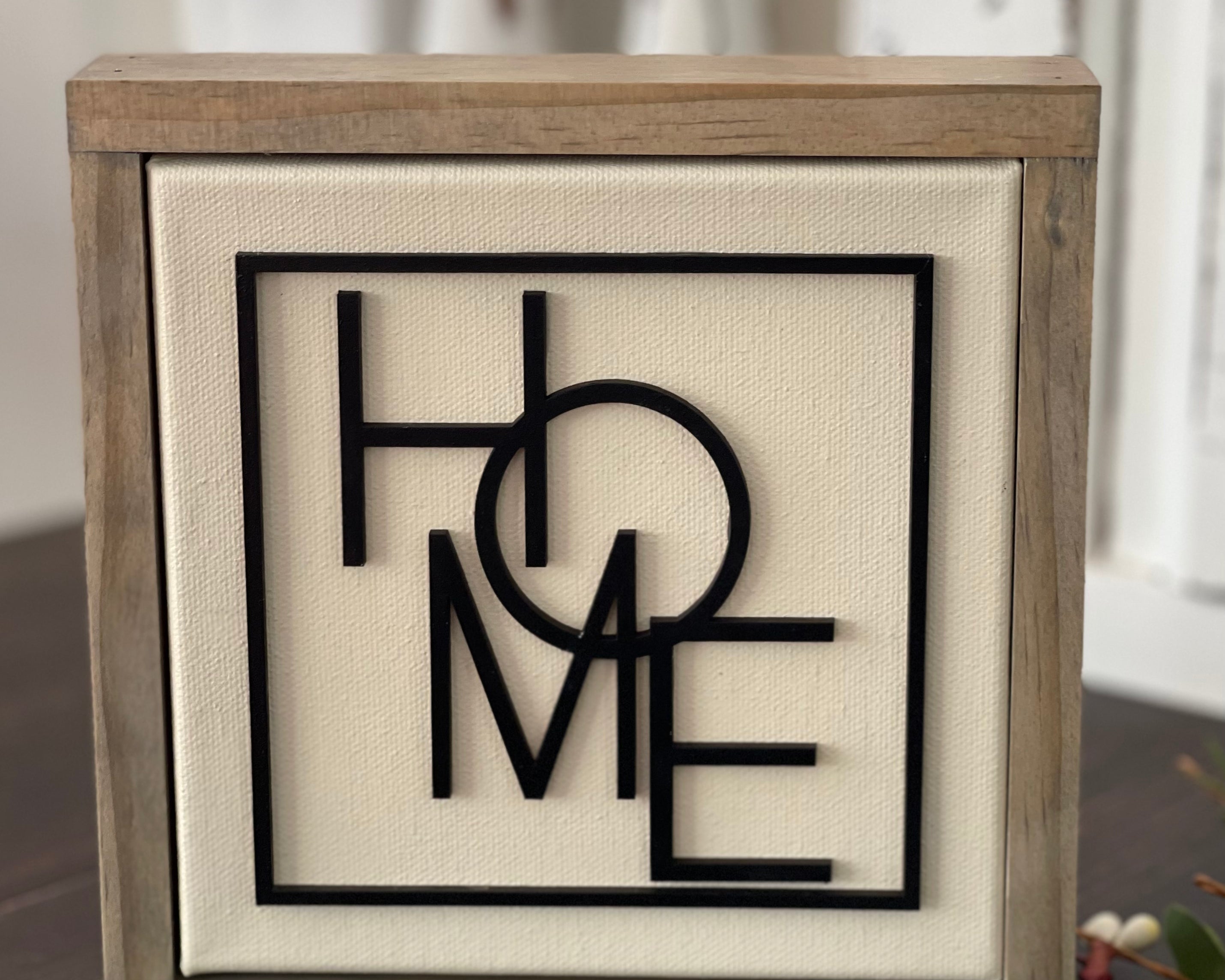 This image shows the Home canvas sign standing up on a bench surrounded by greenery.