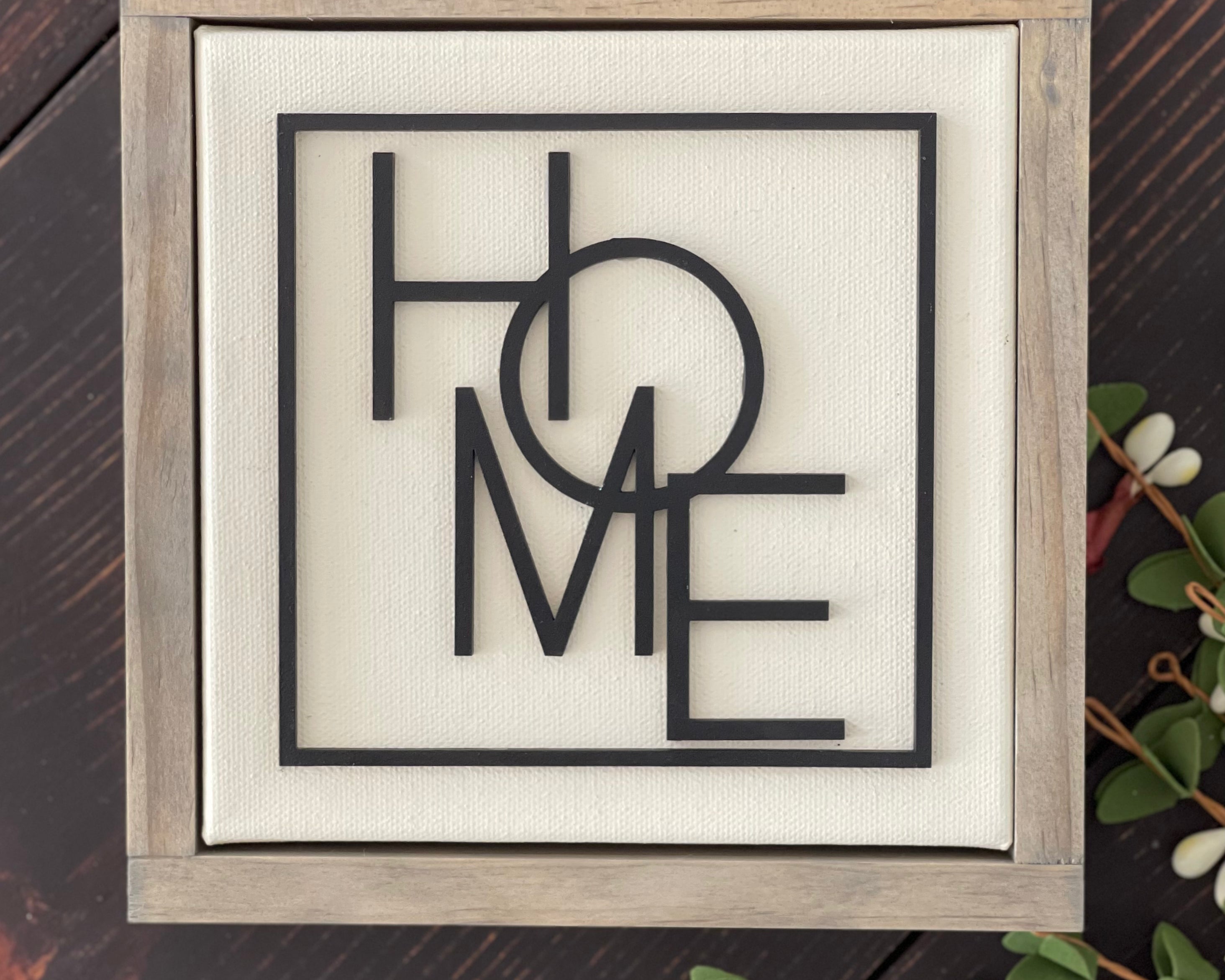 This Home sign is displayed laying on a bench with greenery.