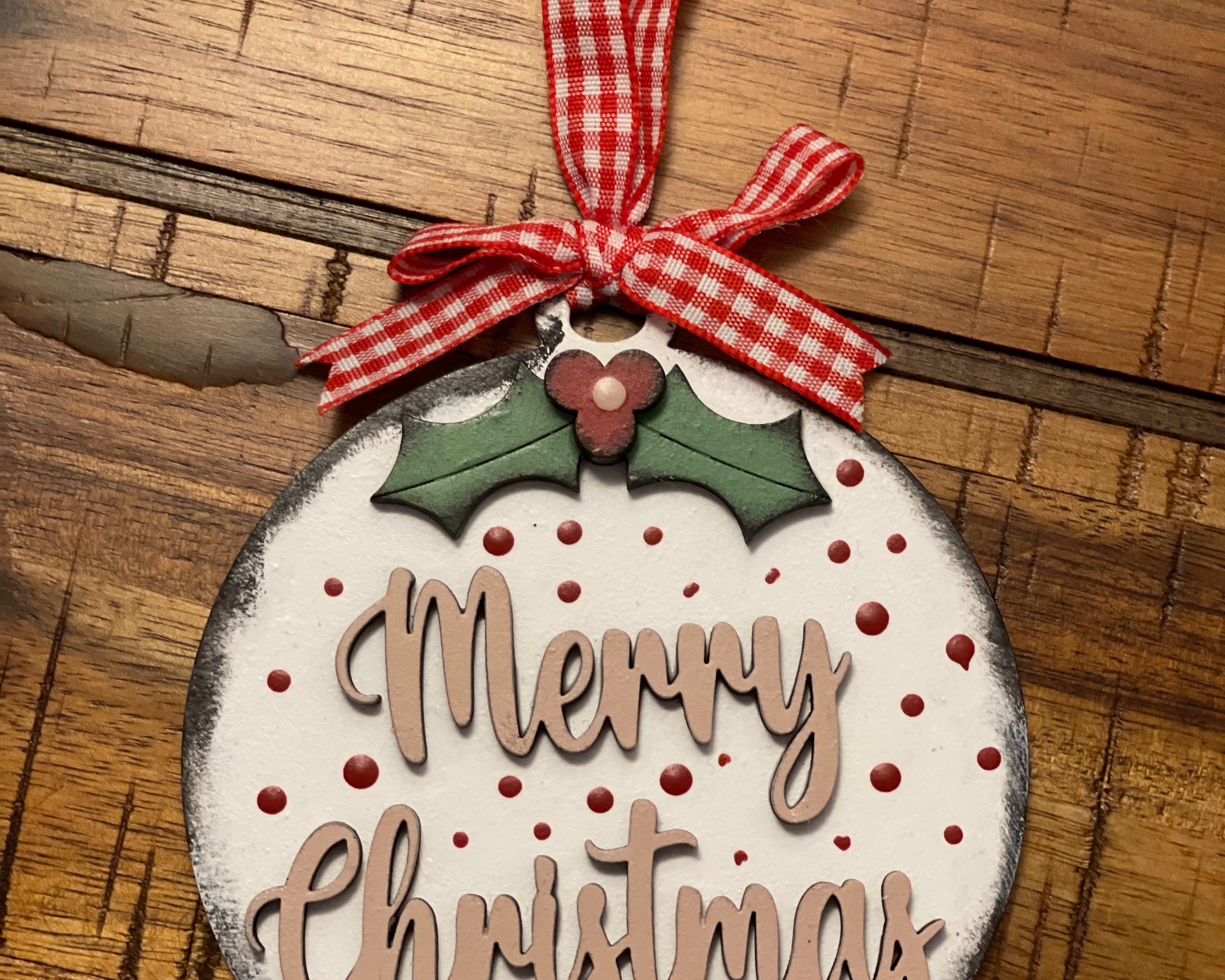 Merry Christmas ornament is displayed on a wood table.