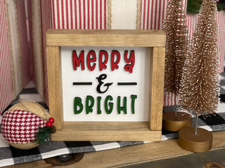 Merry & Bright 3D laser wood cut out sign has the words merry in red, & in black, and bright in green.  The frame is natural stain making the words pop!