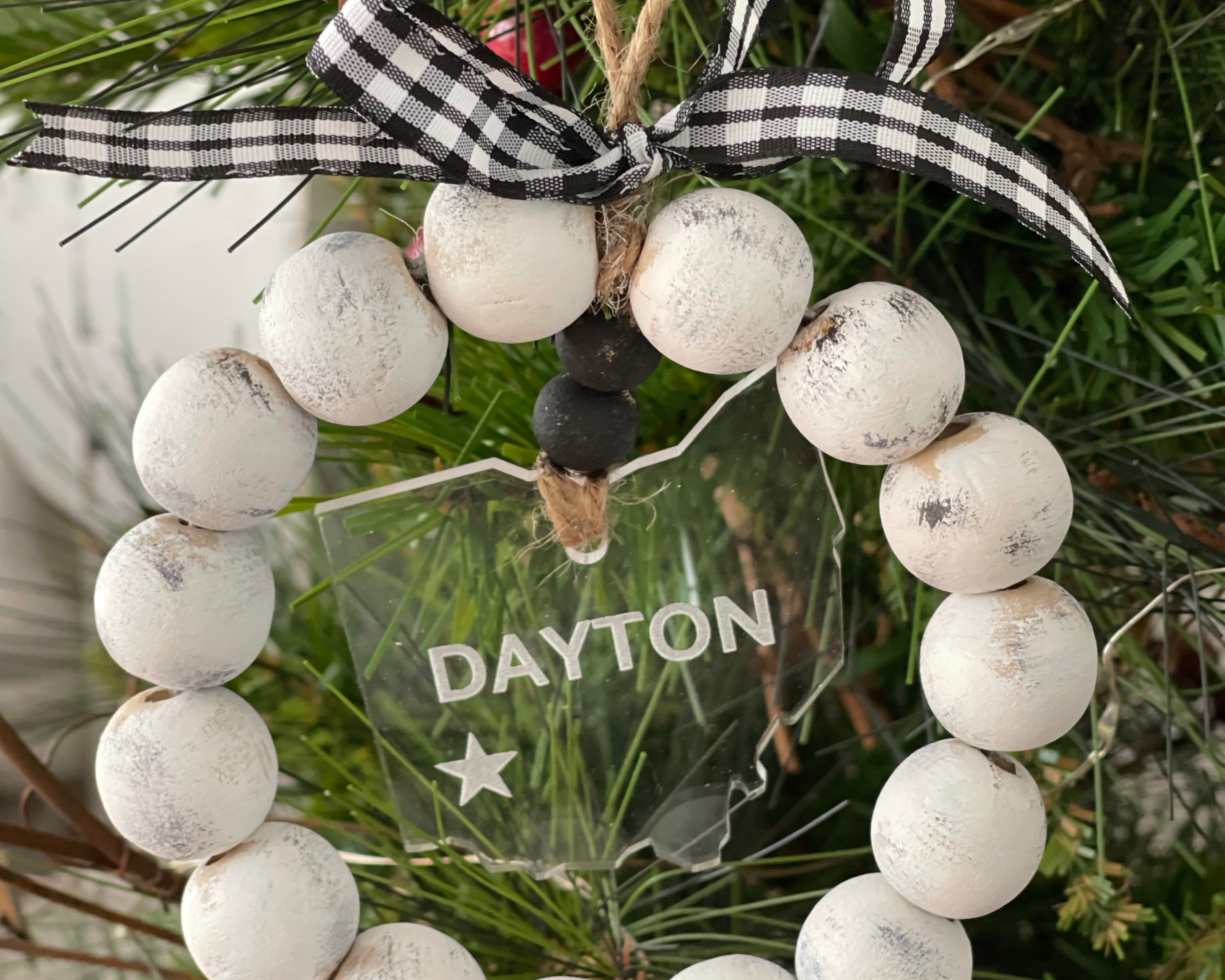 This distressed beaded wreath ornament is showing the state of Ohio and the city of Dayton cut and engraved on clear acrylic.  A red and black plaid ribbon finishes this look.