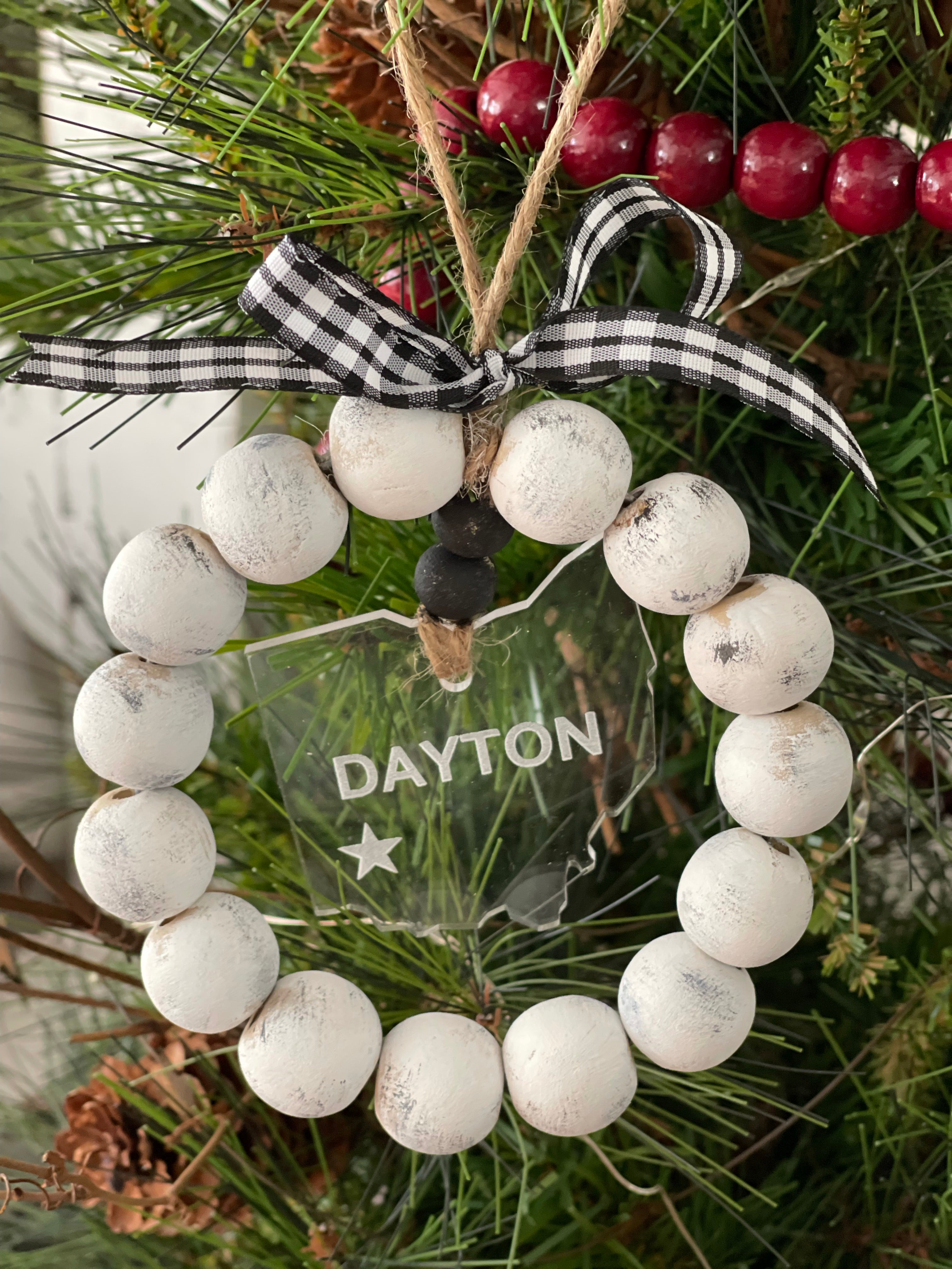 This distressed beaded wreath ornament is showing the state of Ohio and the city of Dayton cut and engraved on clear acrylic.  A red and black plaid ribbon finishes this look.