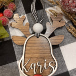 This ornament shows a walnut base with white 3D wood and a name. Buffalo plaid ribbon and a red nose.