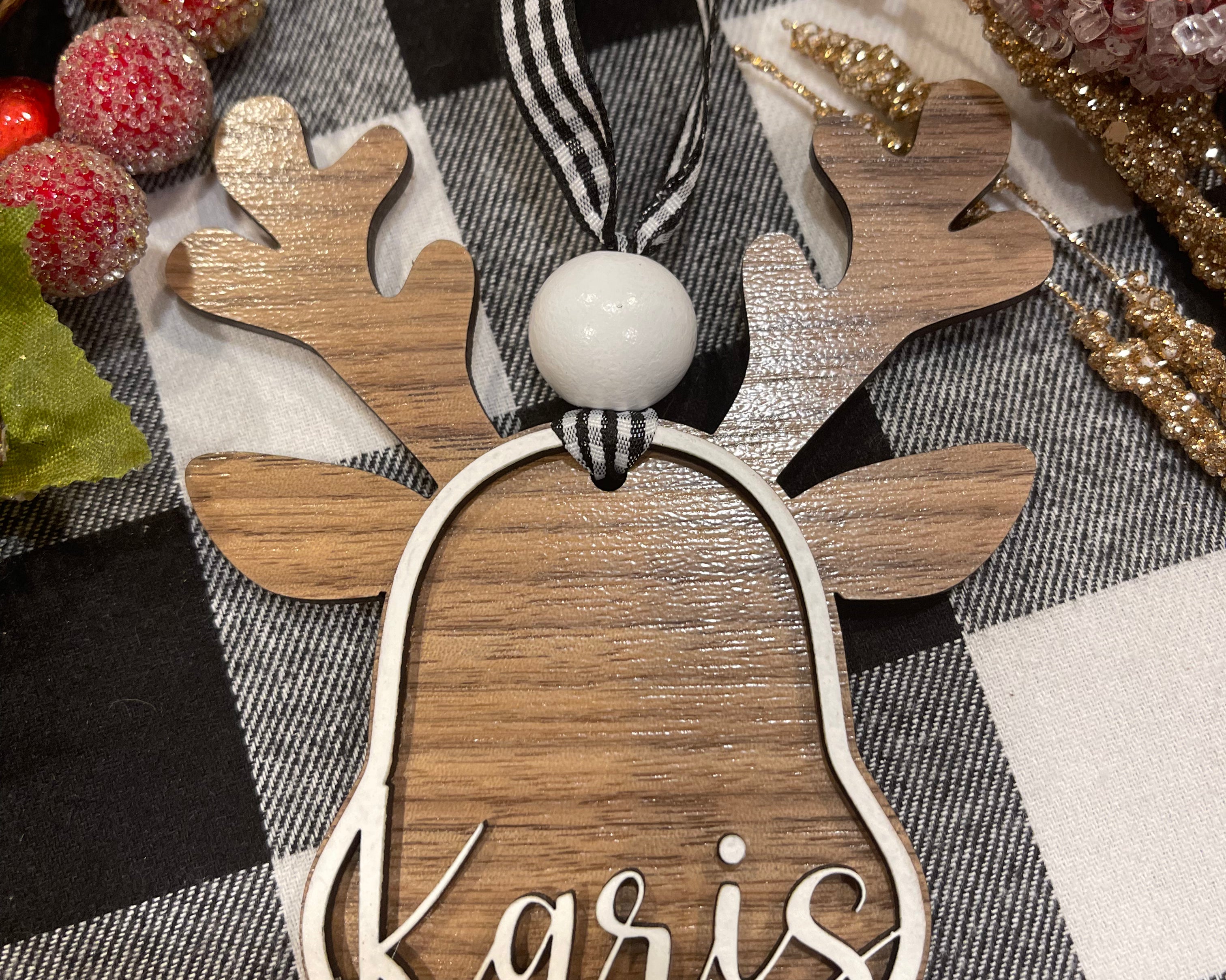 This ornament shows a walnut base with white 3D wood and a name. Buffalo plaid ribbon and a red nose.