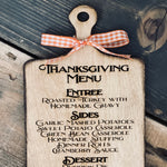 This image shows the engraved thanksgiving menu cutting board with an orange ad white plaid ribbon.