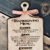 This image shows the engraved thanksgiving menu cutting board with an orange ad white plaid ribbon.