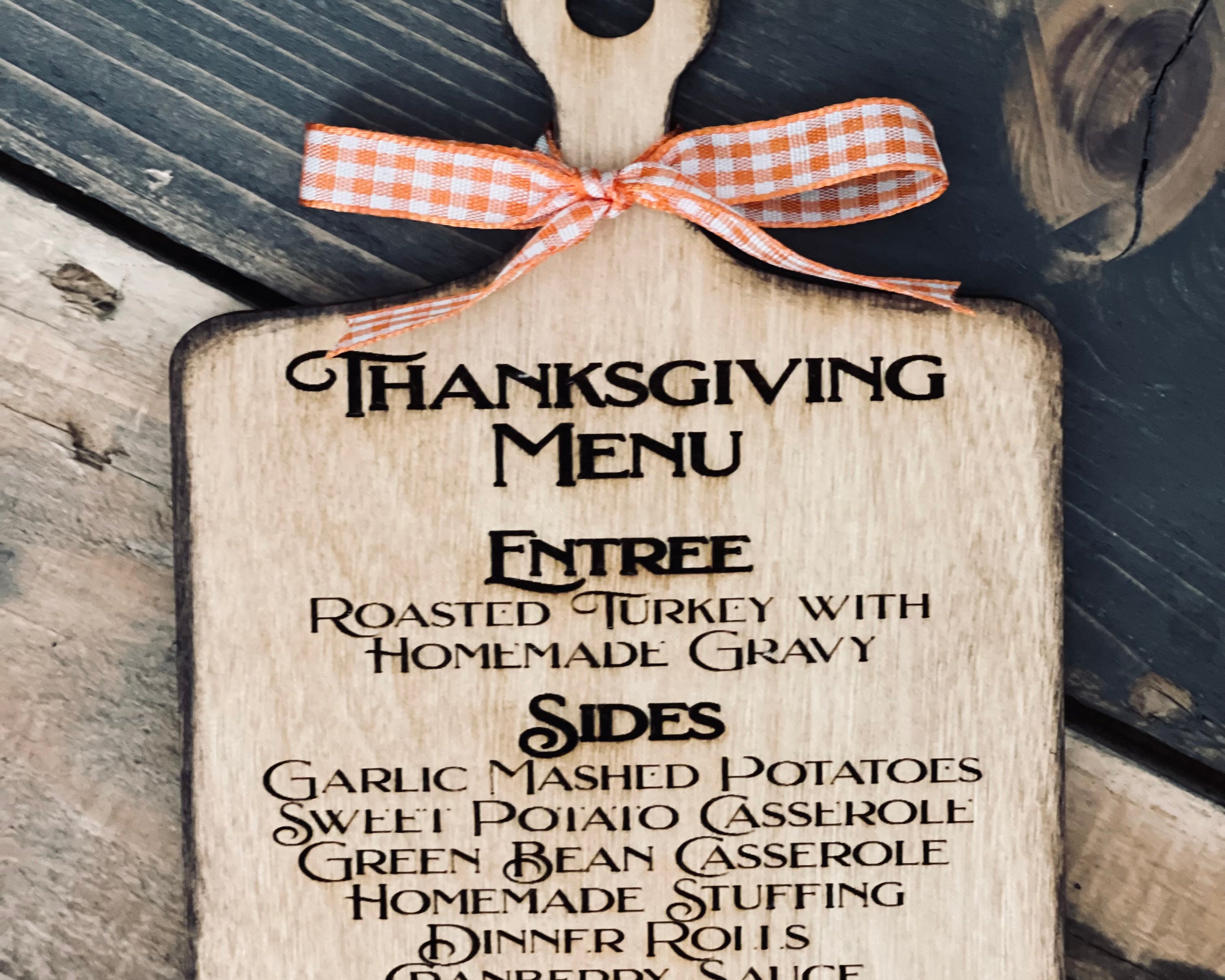 This image shows the engraved thanksgiving menu cutting board with an orange ad white plaid ribbon.
