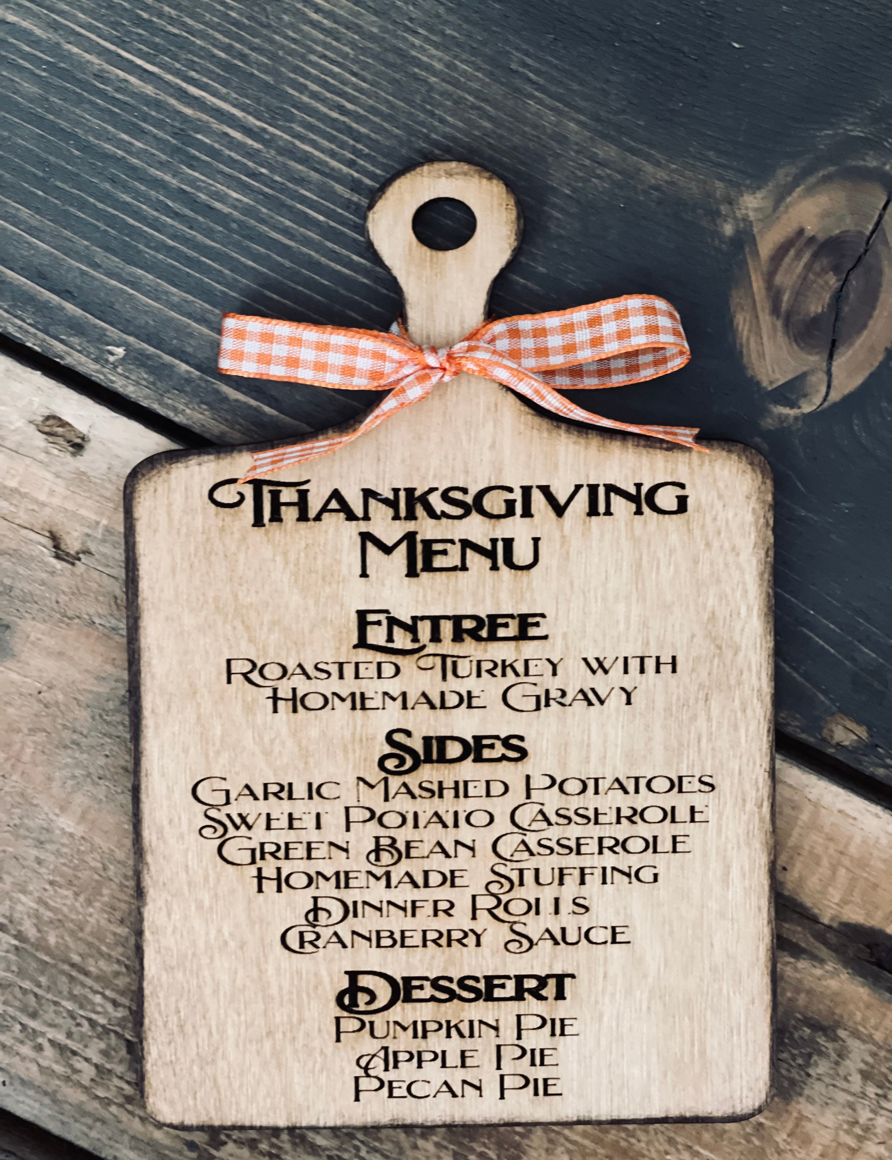This image shows the engraved thanksgiving menu cutting board with an orange ad white plaid ribbon.