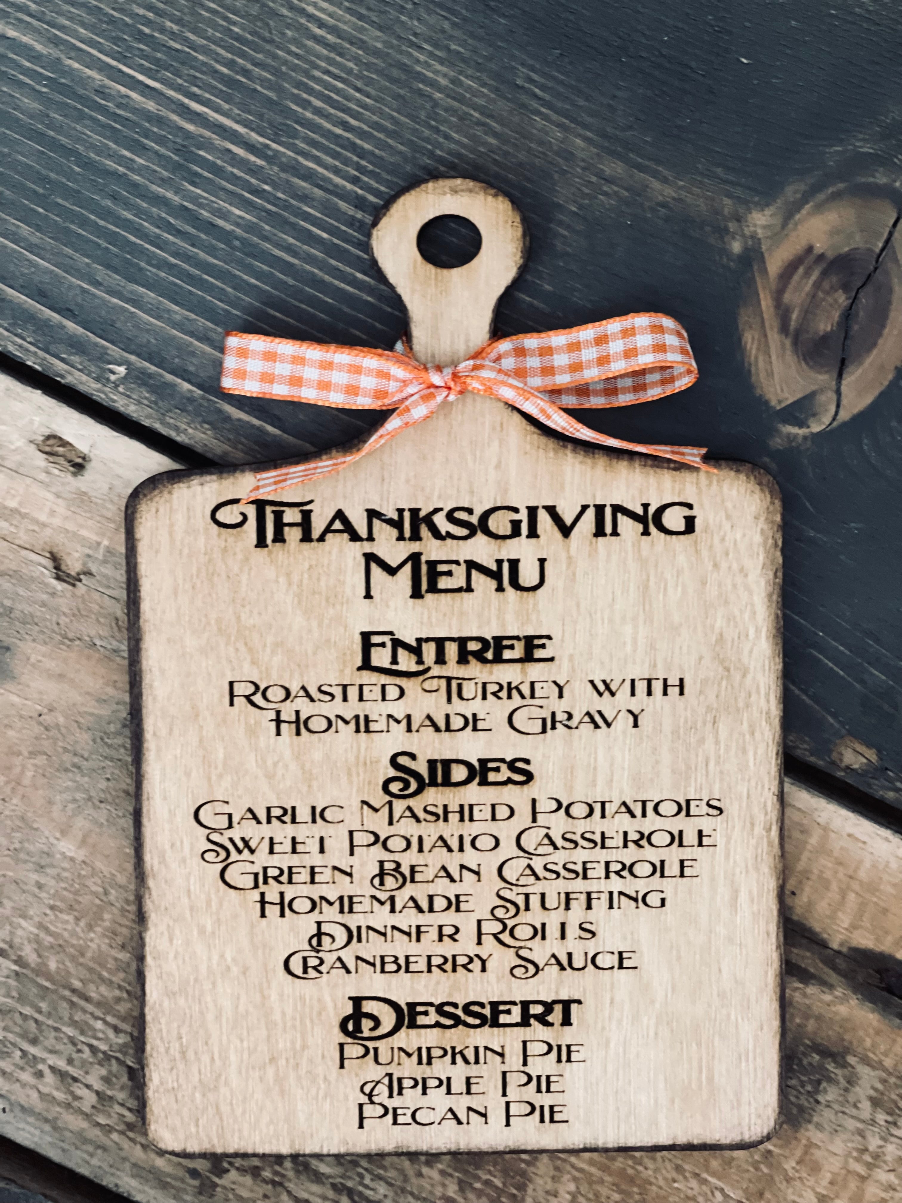 This image shows the engraved thanksgiving menu cutting board with an orange ad white plaid ribbon.