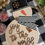 This image shows the large tan snowman that says joy to the world in script.