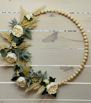 This 24" wood beaded wreath is adorned with white peony faux flowres, mini roses, lambs ear and dried wheat stems.  Add this to any room or on the inside of your front door.  Not recommended to hang directly in outdoor elements.